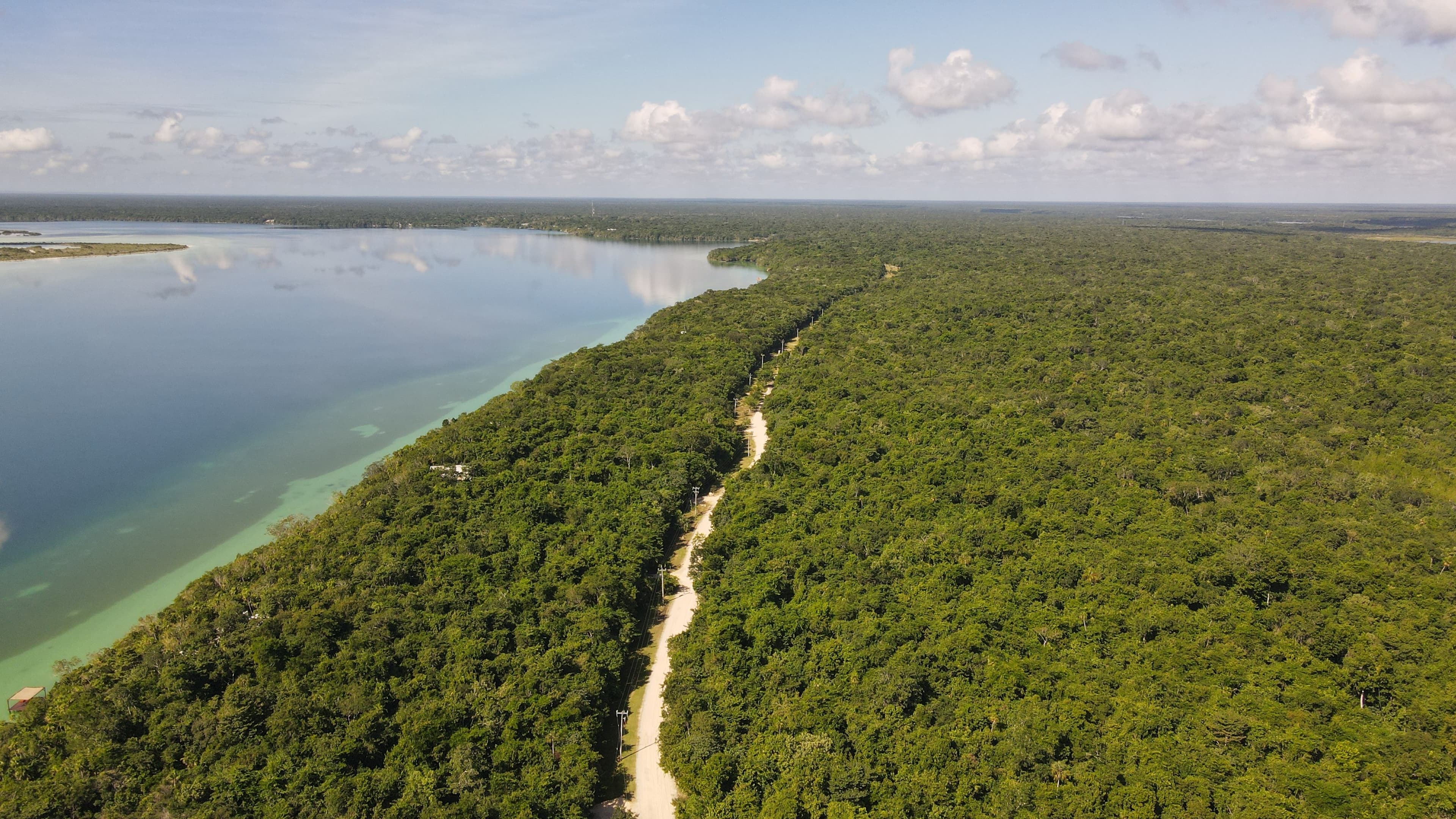 Aerial view of the sand access road running through jungle along the Bacalar lagoon shoreline